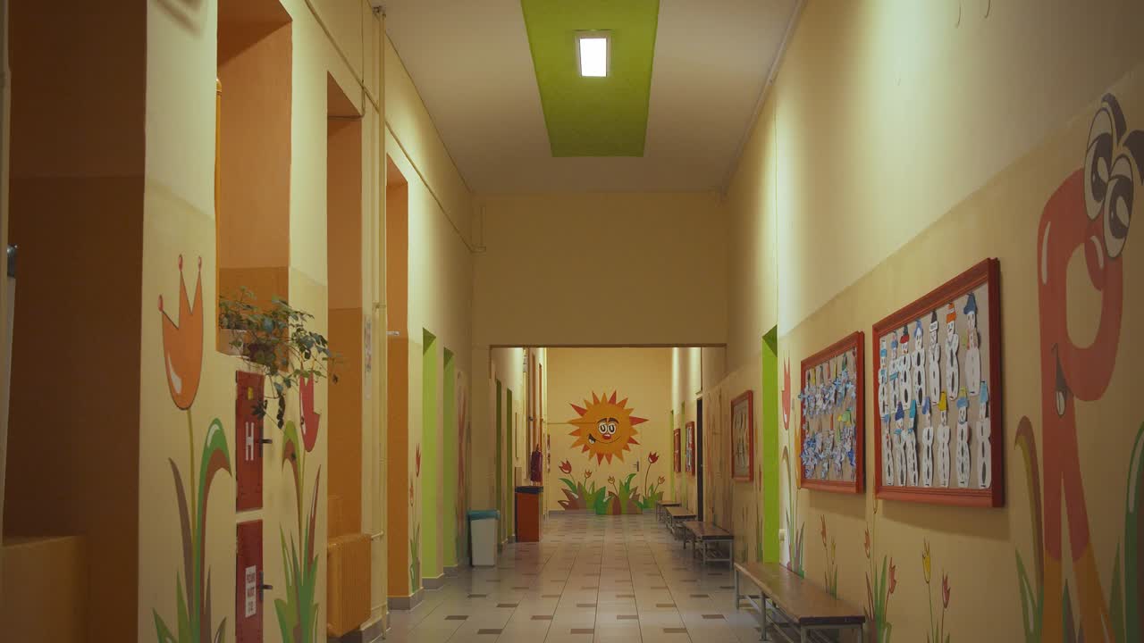 An empty school hallway in the dark suddenly illuminates from the switched-on fluorescent lamps and reveals paints on the walls
