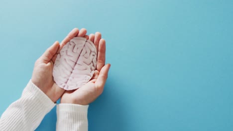 Video-of-hands-holding-brain-on-blue-background-with-copy-space