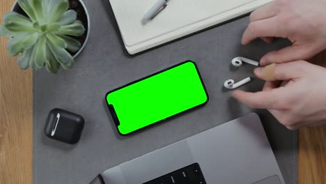 a man takes wireless headphones lying next to a smartphone with a green screen