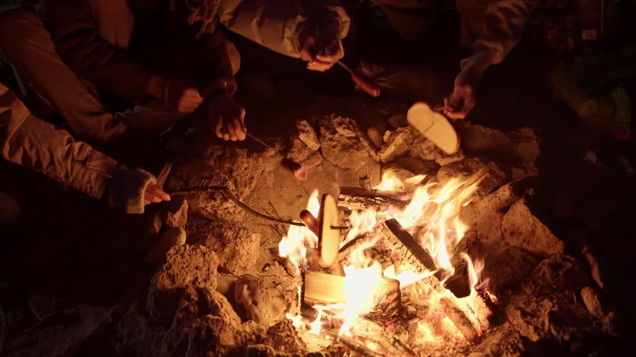 Friends Roasting Hot Dogs Around a Campfire at Night