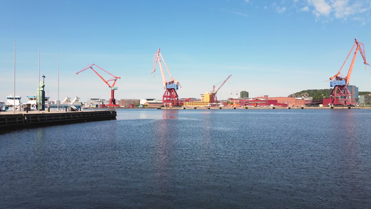 낮에 스웨덴 예테보리의 산업 항구에 있는 부둣가 갠트리 크레인의 전망과 함께 물 위를 날고 있는 드론 - 낮은 공중