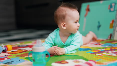 playful sweet kid lies on belly waving feet. tiny child stretches arm to take a bottle. beautiful baby sticking out his tongue.