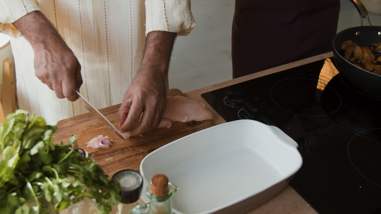 Hands cutting raw chicken on a cutting board in the kitchen