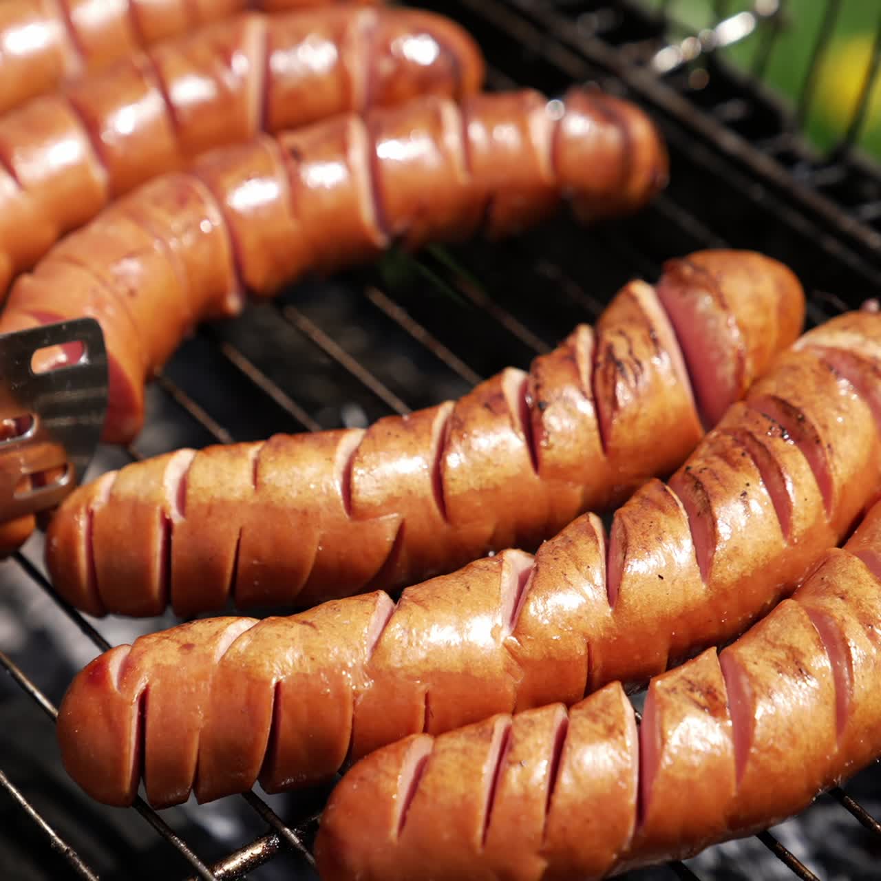 Hot tasty sausages on grill. Cook turning over almost ready sausages for the picnic. Frying food on charcoals in the garden. Close-up