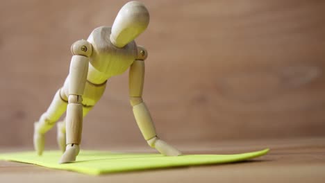 estatuilla de madera haciendo ejercicios de empuje en una alfombra de ejercicio contra un fondo de madera