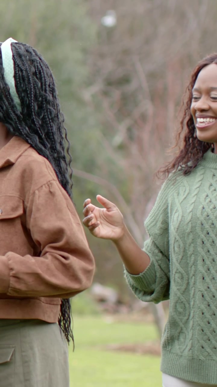Vertical video: Coming woman in green helping girl touching hair walking in park girl holding panel