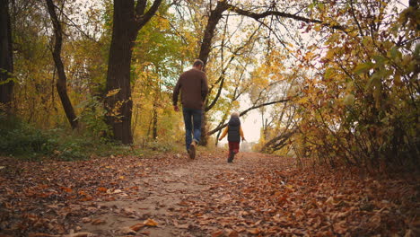 Niño-Feliz-Y-Padre-En-El-Bosque-De-Otoño-Corriendo-Sobre-El-Camino-Cubierto-De-Follaje-Seco-El-Hombre-Está-Atrapando-A-Su-Hijo-Y-Girando-Feliz-Fin-De-Semana-Familiar-En-La-Naturaleza