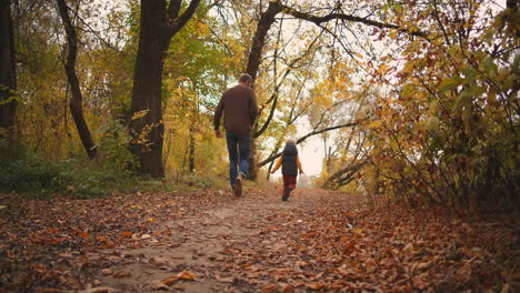 hijo feliz y padre en el bosque de otoño corriendo por el camino cubierto de follaje seco hombre está atrapando hijo y girando feliz fin de semana familiar en la naturaleza