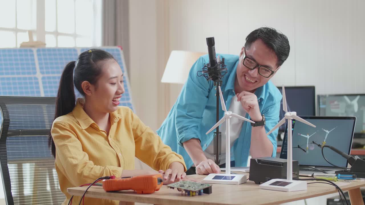 행복한 아시아 남녀가 사무실에서 태양전지 에 노트북으로 작업하는 동안 풍력 터빈을 성공적으로 테스트합니다.