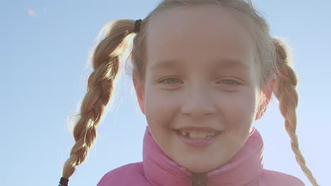 a small braided blonde smiles at the camera and reveals the gaps between her teeth