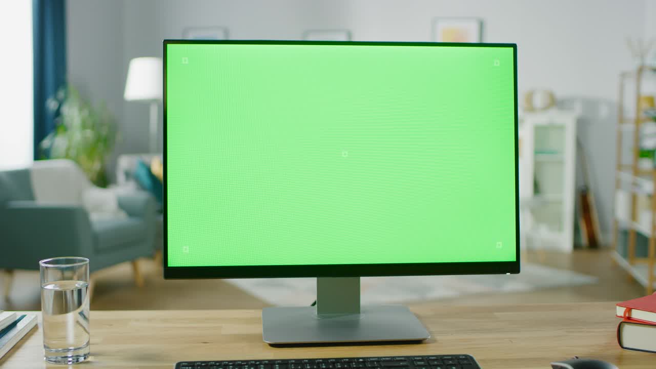 una computadora personal moderna con pantalla de maqueta verde de pie en el escritorio en la acogedora sala de estar. un hombre con teléfono móvil camina a través de su apartamento.