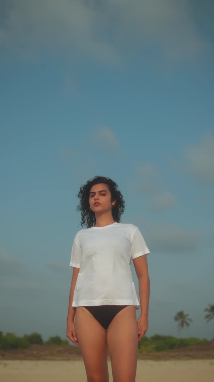 Confident woman standing on the beach, looking toward the horizon under blue skies