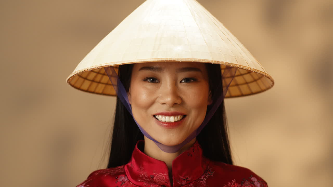 빨간 옷을 입은 젊은 아시아 행복한 여성과 카메라를 보며 즐겁게 웃고 있는 코누스 모자의 클로즈업 보기