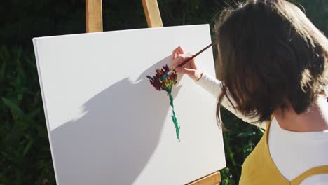 caucasian woman with brown hair painting in sunny garden