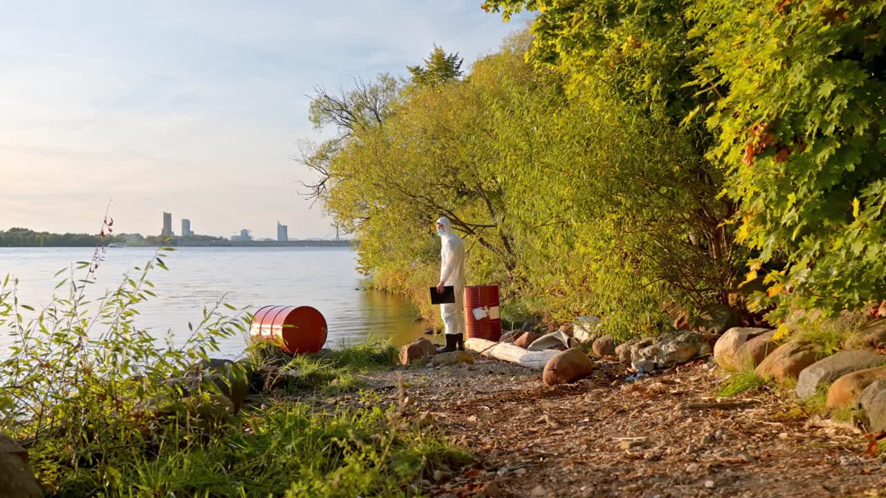 Scientist in hazmat coveralls walks dump site near lake during pollution inspection