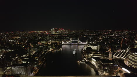 Backwards-fly-above-Thames-river.-Aerial-view-of-white-colour-illuminated-Tower-Bridge.-Revealing-of-Shard-skyscraper.-London,-UK