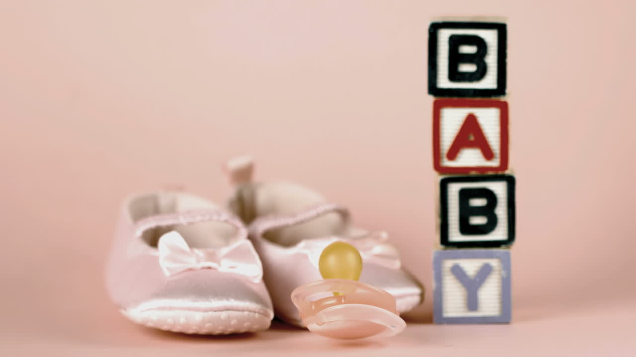 Pink soother falling in front of baby shoes and baby blocks