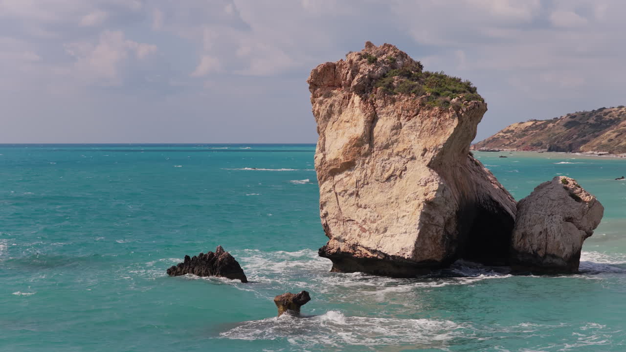 Veduta aerea con drone di una singola grande roccia che emerge da acque limpide color turchese con onde leggere nel Mar Mediterraneo a Cipro