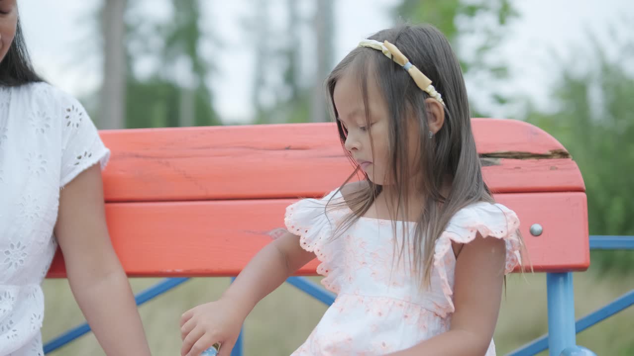 임신 한 어머니 와 어린 딸 은 나무 와 초록색 으로 둘러싸인 공원 의 놀이터 에서 함께 놀이 를 즐긴다