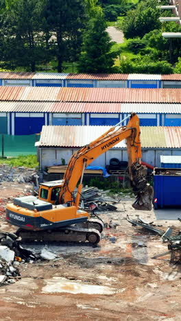 heavy machinery at site. a yellow excavator is demolishing structures at a busy construction site under a clear sky