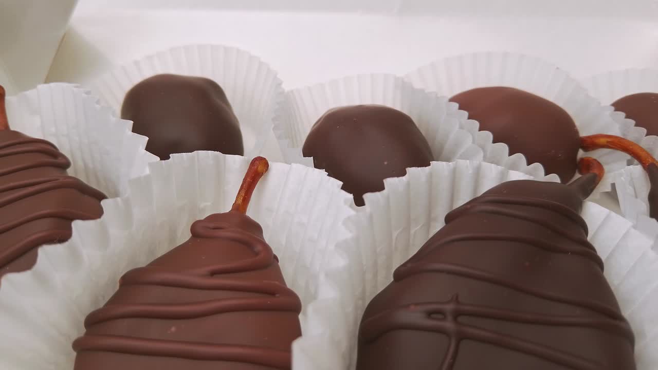peras secas y dátiles en chocolate. caramelos de chocolate en caja de regalo de primer plano extremo. 4k imágenes de primer plano de la cámara moviéndose lentamente entre chocolates variados confitería en el fondo blanco