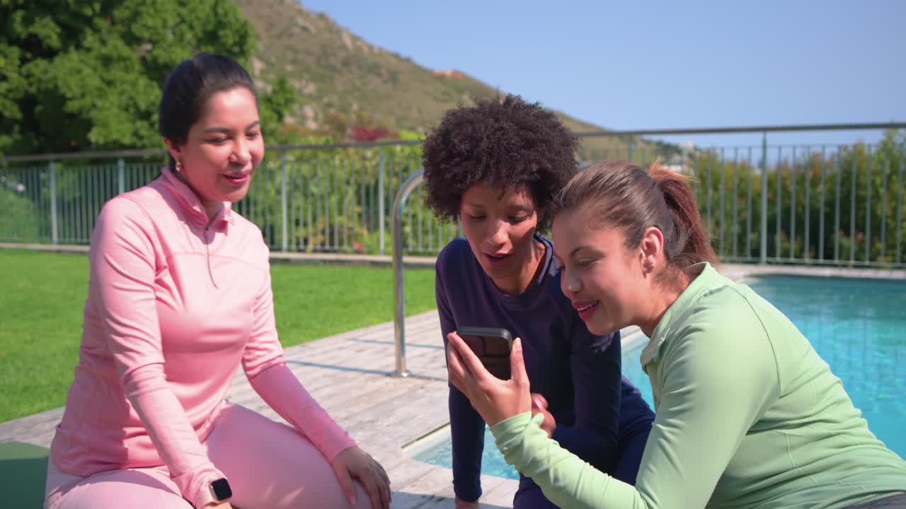 Spotting phone, Diverse female friends in sportswear pointing, posing poolside reviewing photos