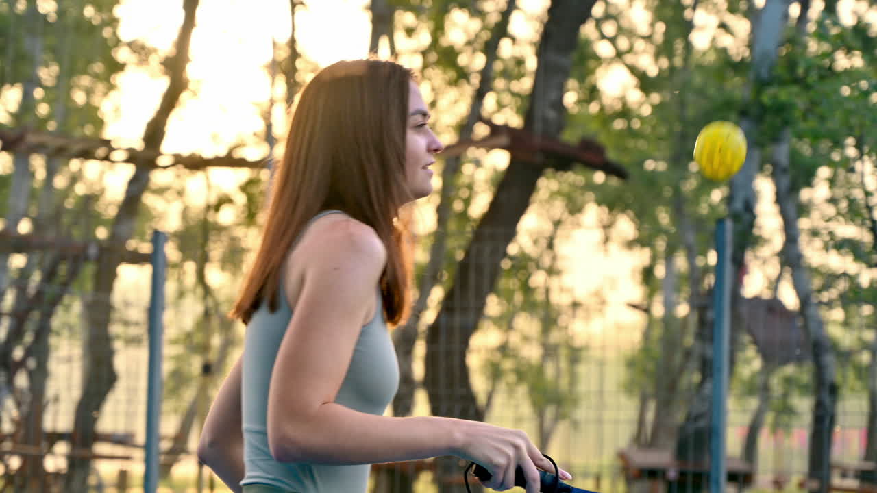 Woman playing pickleball on a blue and green court at sunrise, after rain