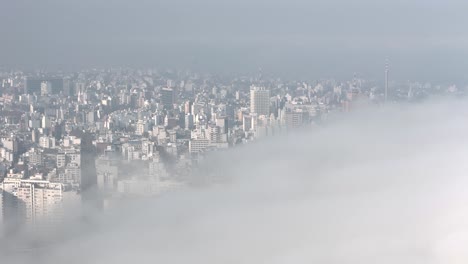 aerial drone smoothly navigates montevideo as thick fog advances, wrapping towers and streets in a soft white veil