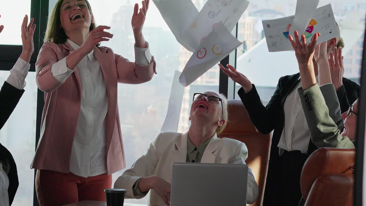 다양한 색의 비즈니스 옷과 재을 입은 행복한 비즈니스 여성 그룹은 현대적인 사무실에서 그들의 승리와 성공의 이름으로 비즈니스 문서와 종이를 던집니다.