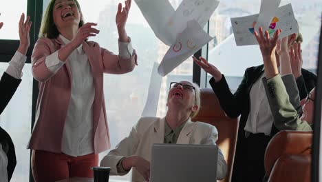 un grupo de mujeres de negocios felices con ropa de negocios y chaquetas de diferentes colores lanzan documentos de negocios y hojas de papel en nombre de su victoria y éxito en una oficina moderna