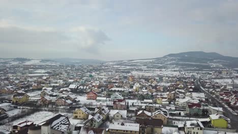 Drone-Volando-Sobre-Los-Suburbios-De-La-Ciudad-Con-Casas-Coloridas-Y-Techos-Cubiertos-De-Nieve,-Bistrita,-Rumania,-Movimiento-De-Muñeca-Hacia-Adelante