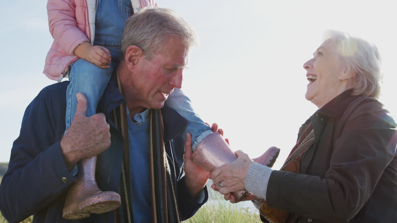 할머니는 할아버지가 그녀의 어깨에 타는 동안 손녀를 입히고 있습니다.