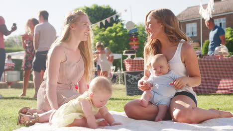 Slow-Motion-Shot-Of-Two-Mothers-Sitting-On-Rug-And-Playing-With-Babies-At-Summer-Garden-Fete