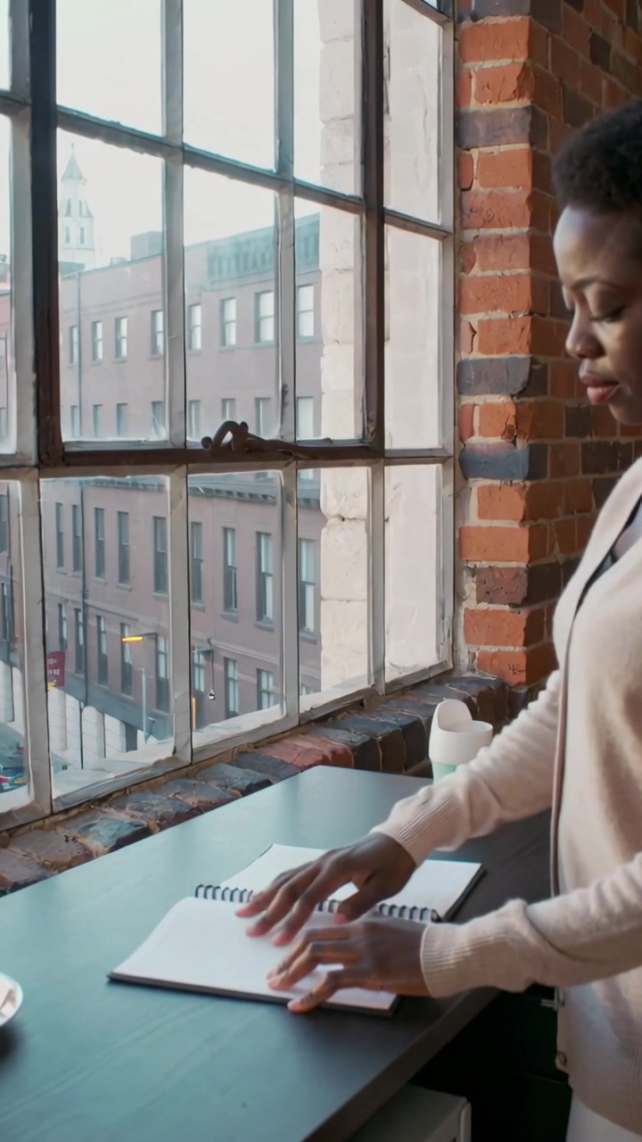 Vertical video: Placing notebook, woman in sweater flipping pages, studying in loft, copy space