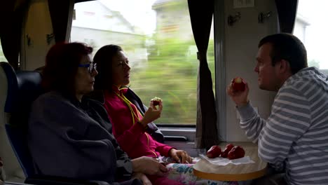 a man and women are sitting on the train, eating malayan apples and talking