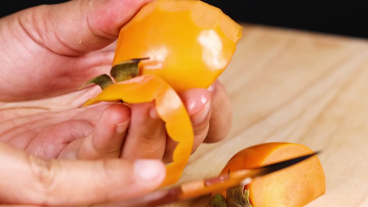 Hænder skræller omhyggeligt en moden persimmon