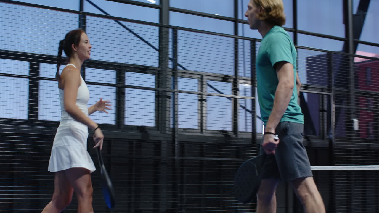 Young diverse athletes discussing padel tennis strategy on indoor court, holding rackets confidently