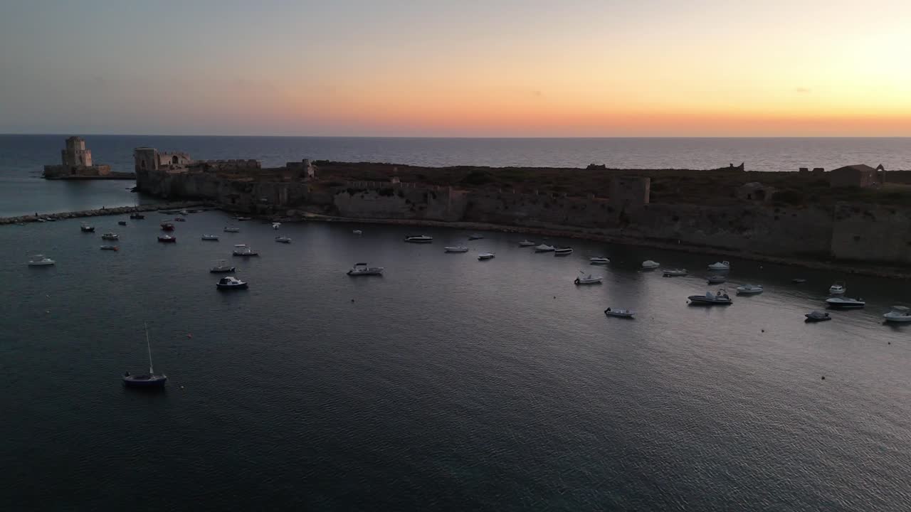 Methoni,Messenia,Peloponnese,Aerial view forward along Methoni Castle towards Bourtzi tower during sunset.Colorful sky and dark blue sea.Lot of small boats in the bay all along the castle