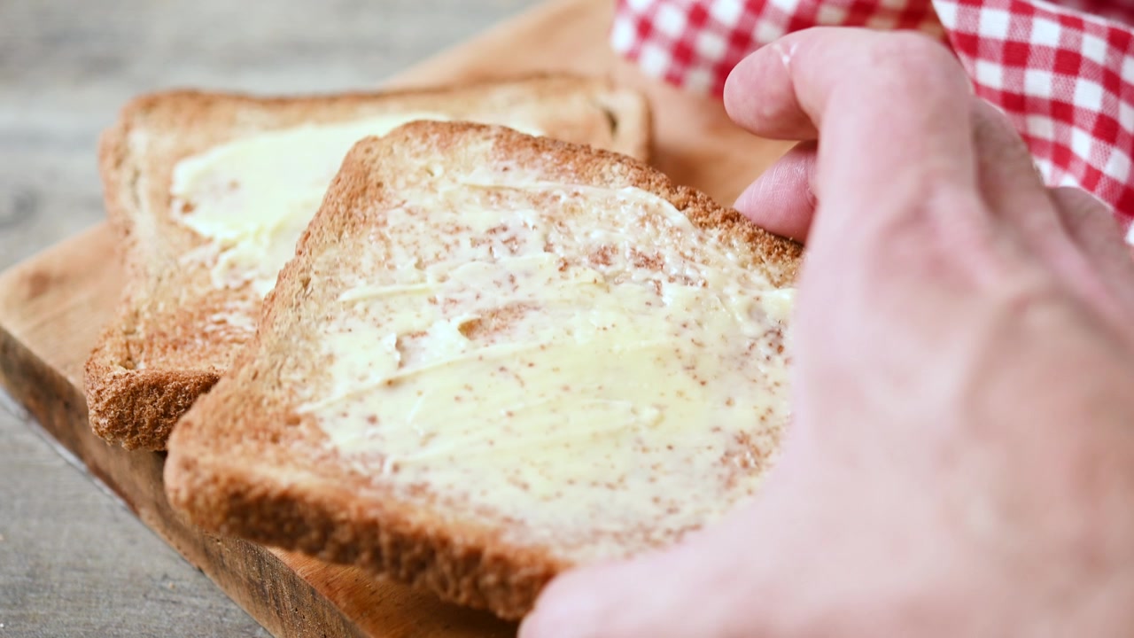 Mano che posiziona una fetta di toast imburrato su un tagliere di legno