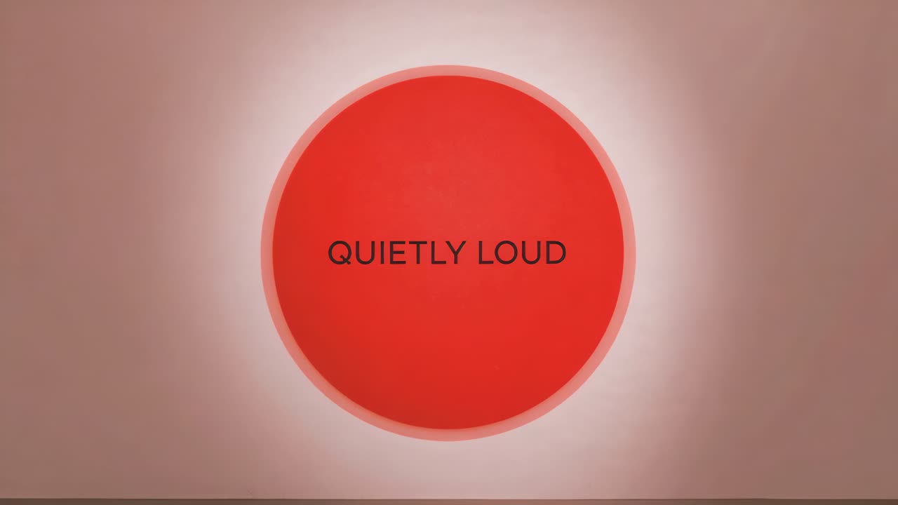 Animating red circular disc pulsing halo on muted pink backdrop showing QUIETLY LOUD drawing focus