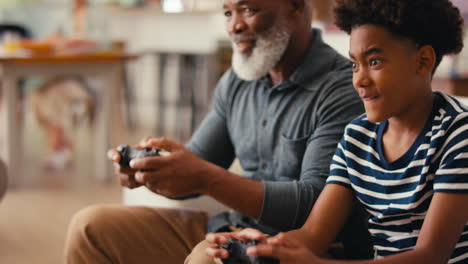 abuelo y nieto sentados en el sofá en casa jugando videojuegos juntos