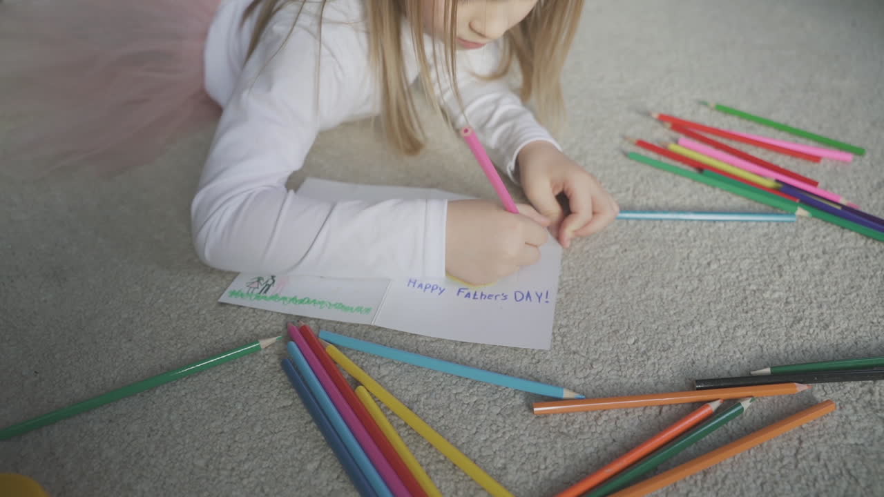 pequeña hija escribiendo y dibujando una tarjeta de felicitación para papá