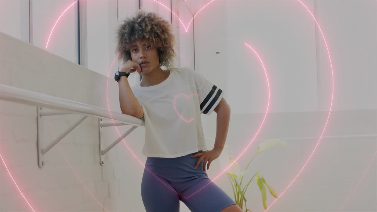 Leaning on ballet barre, woman surrounded by heart-shaped animation in dance studio