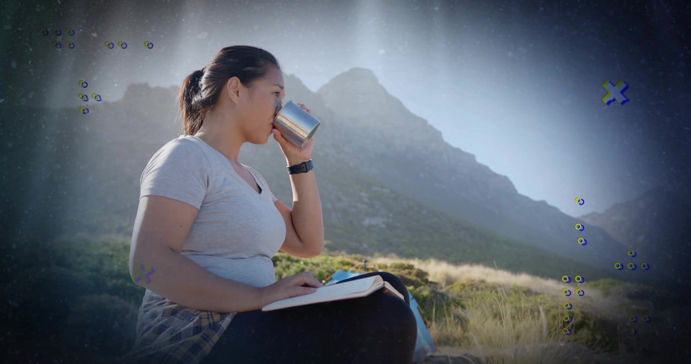 Mulher levando caneca aos lábios, começando a escrever no caderno, refletindo na encosta para seu diário de viagem