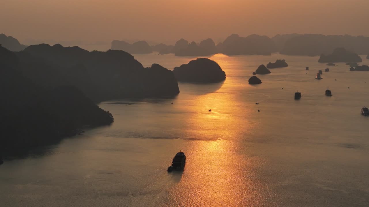 Drone video captures Ha Long Bay's majestic limestone cliffs at sunset, with golden light reflecting on the tranquil waters, creating a serene, picturesque landscape