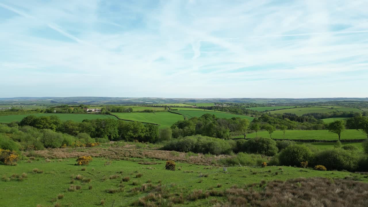 Aerial view over the South Downs, West Sussex, showcasing rolling green fields, hedgerows, and scattered farm buildings beneath a clear sky with light contrails across the rural English landscape