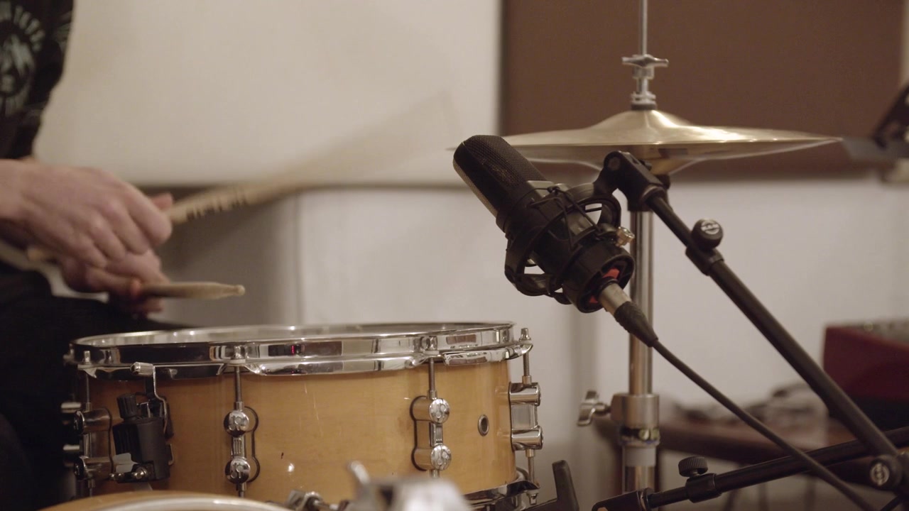 Drummer playing drum groove in a recording studio with microphones