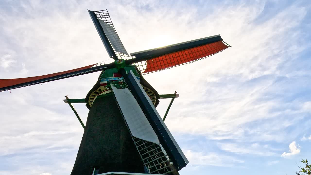 Low-angle view of historic windmill blades turning, strong sunlight, clear sky, smooth camera movement