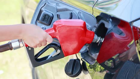 a person refuels a vehicle at a gas station using a red fuel nozzle in daylight