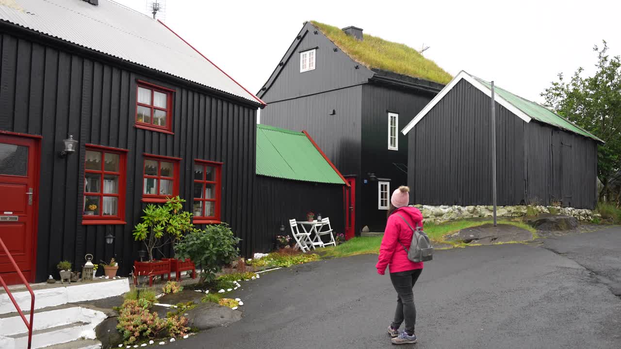mujer mirando casas de madera negras con techos de alquitrán y césped en torshavn